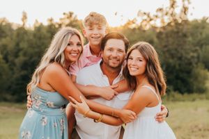 A family embracing in casual attire during sunset photoshoot in field.