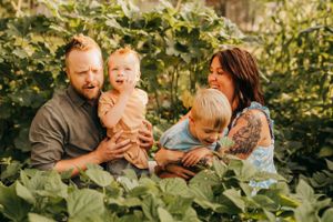 Family spending time together among lush garden greenery in warm sunlight.