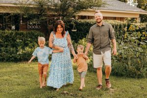 Family of four walking together in a garden on a bright summer day.