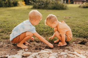 Two young children crouching down to explore something in the dirt on a sunny day.