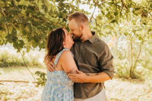 A couple sharing an intimate moment under green foliage during a photoshoot.