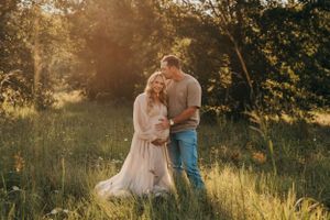 Romantic couple embracing in sunlit meadow during golden hour maternity photo session.