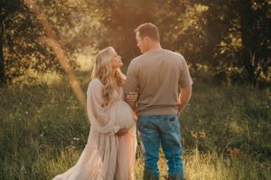 Couple holding hands in scenic field during sunset maternity photography session.