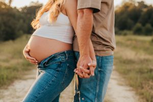 Close-up of expecting couple holding hands showing baby bump in casual attire.