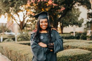 Graduate in cap and gown smiling during outdoor graduation photoshoot at sunset.