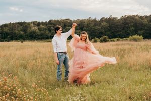 Couple dancing in field during sunset maternity photoshoot with flowing pink dress.