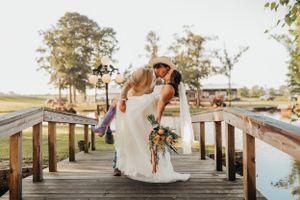 Wedding couple sharing a dip kiss moment on a wooden pier at sunset during their wedding celebration.