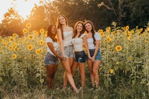 Group of friends posing together in sunflower field during golden sunset.