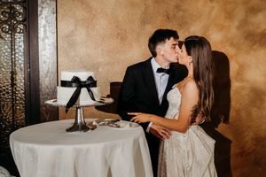 A couple in formal attire shares an intimate moment while dining at an elegant table with rustic walls in the background.