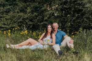 Couple sitting together in a lush green meadow with yellow wildflowers, smiling outdoors.
