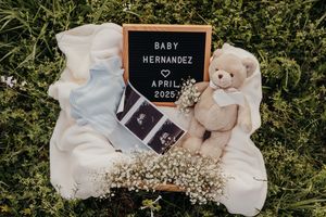 A pregnancy announcement display with baby items, ultrasound photos and letter board on green grass background.