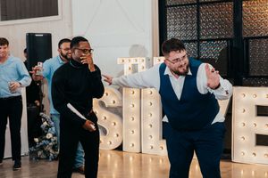 A group of people dancing and celebrating at an indoor wedding reception with illuminated letter decor.