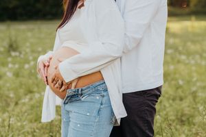A couple in casual clothing embraces while standing in a wildflower meadow on a sunny day.