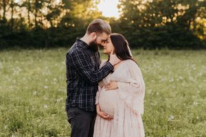 A romantic moment between an expectant couple sharing a tender embrace in a sunlit meadow at golden hour.