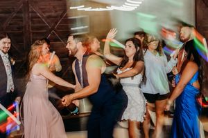 Guests dancing and celebrating energetically on a wedding reception dance floor with colorful lighting effects.