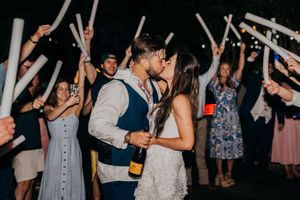 Newlyweds kiss during their sparkler send-off exit as wedding guests line the pathway holding illuminated sparklers.