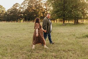 Two people walk hand in hand through a sunlit meadow at golden hour wearing casual autumn attire.