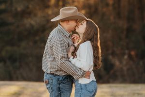 Romantic western-styled couple embracing under warm sunset lighting.