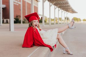 Model wearing a red blazer and silver heels poses during fashion photoshoot at urban location.