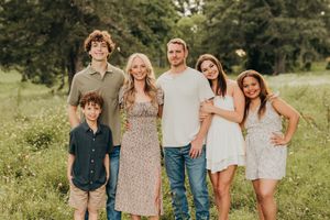 A group gathers together in a sunny field wearing casual summer clothing in warm golden lighting.