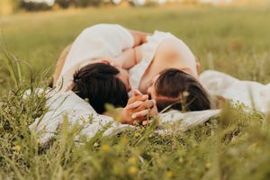 Two people share an intimate moment while resting in tall grass during a warm sunset.