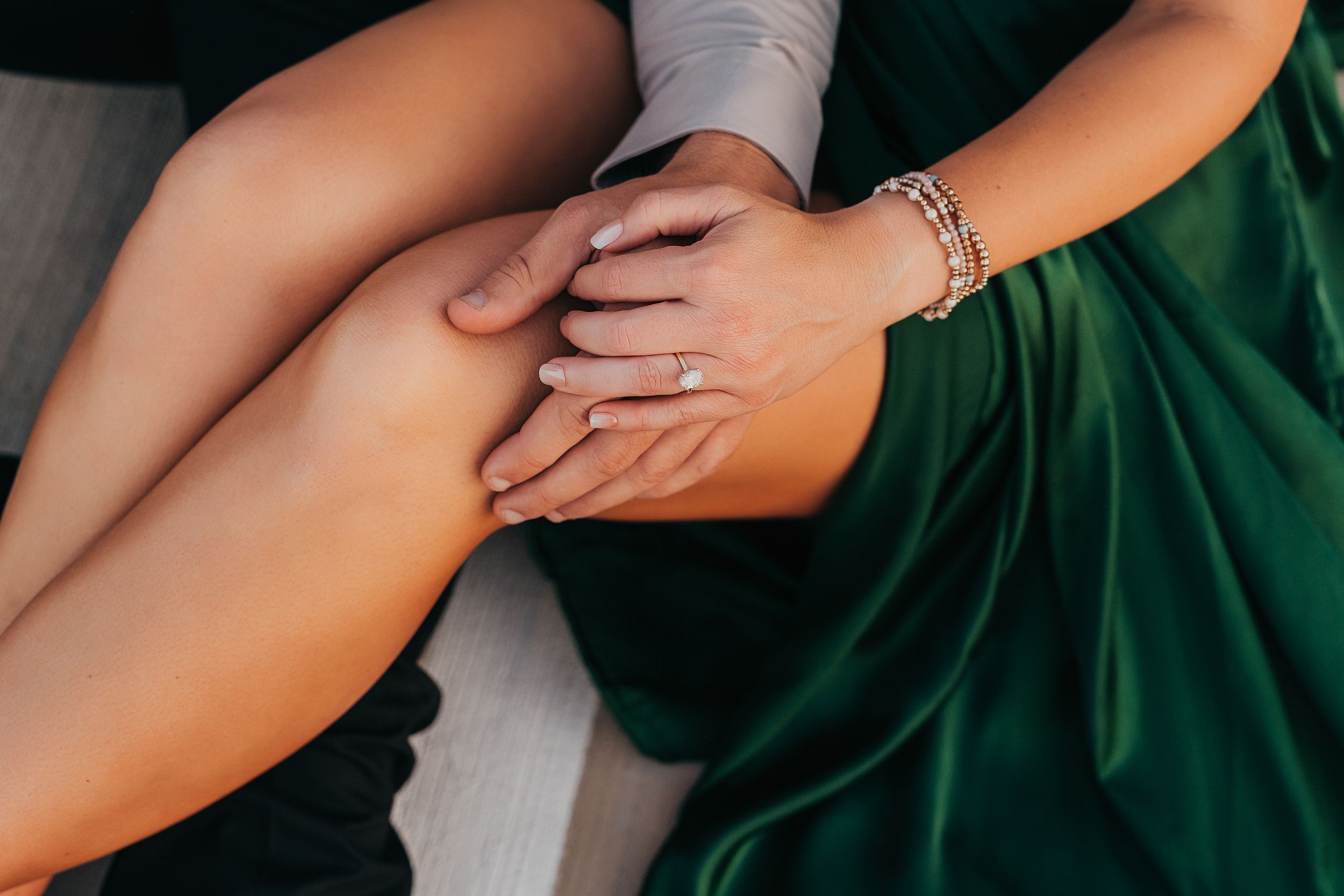 Close-up of couple holding hands, woman wearing green satin dress and gold bracelet.
