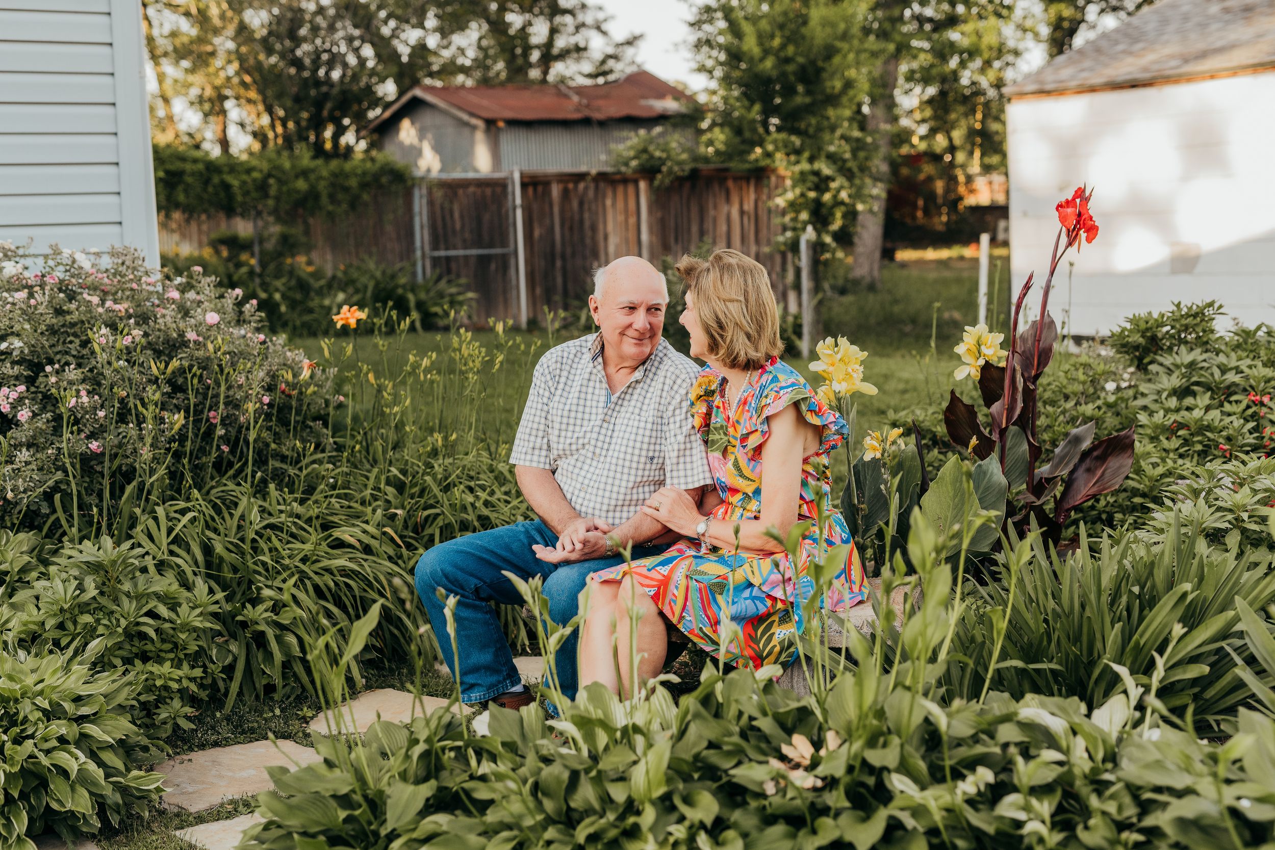 Elderly couple sitting together in a lush garden, sharing a tender moment among colorful flowers.