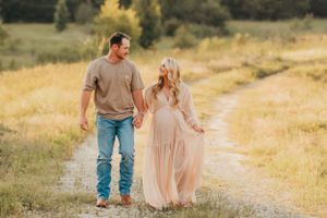 Couple walking hand in hand along countryside path during maternity photoshoot.