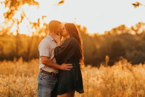 Intimate couple sharing a romantic moment in golden sunlit field at sunset.
