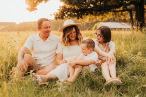 Family sitting together in grassy field during golden sunset hour.