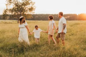 Family walking together hand in hand through sunlit meadow at golden hour.