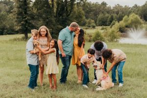 A large family posing with their dogs in a sunny meadow with fountain in background.