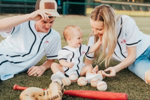 Baseball-themed family photo with baby and sports equipment on grass.