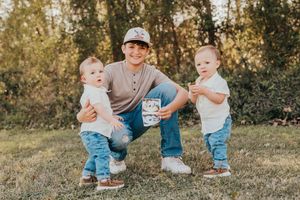 Three people wearing matching denim and casual attire pose together on grass during golden hour outdoor photo session.