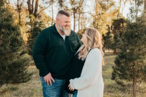 Couple shares loving moment outdoors surrounded by evergreen trees at sunset.