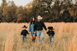 Family walking together through tall autumn grass at sunset holding hands.