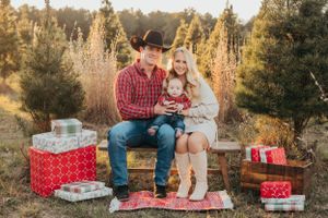 Family in western wear sits on blanket with Christmas presents in rustic outdoor setting.