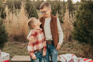 Siblings share tender moment on blanket with Christmas presents in outdoor setting.