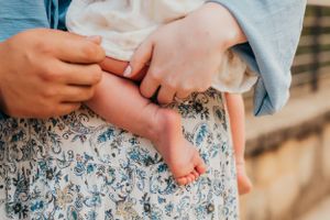 Close-up of hands holding tiny baby feet against floral patterned fabric.