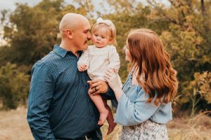 Warm family portrait taken outdoors during golden hour with autumn foliage in the background.