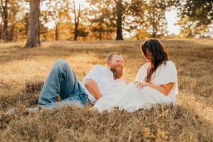Couple relaxing together on grassy hill during golden hour photoshoot.