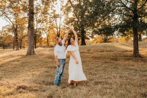 Couple dancing and twirling in a sun-dappled autumn field at sunset.