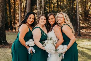 Bride and bridesmaids in emerald green dresses pose together holding white bouquets.