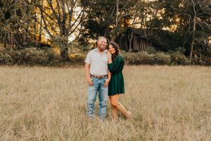 A couple embraces in a golden field during sunset with trees in the background.