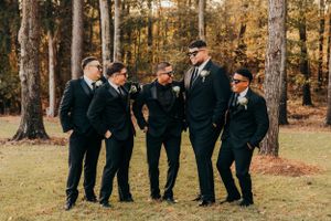 Groomsmen in black suits share a candid moment while posing outdoors.