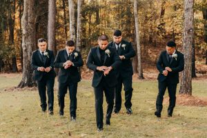 Groomsmen in black suits run playfully across a grassy field during wedding photos.