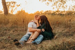 A romantic moment captured between a couple sitting in tall grass during golden hour.