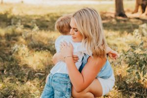 Parent and young child share tender moment outdoors at sunset in golden field.