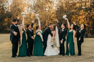 Wedding party in emerald green dresses and black suits celebrating together in front of golden autumn trees.