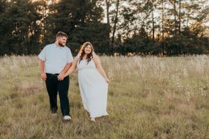 Couple walking hand in hand through tall grass at sunset.